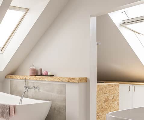 Design de salle de bain sous les combles avec bois OSB Salle de bain sous combles avec baignoire îlot, étagère en bois OSB et fenêtres de toit lumineuses.
